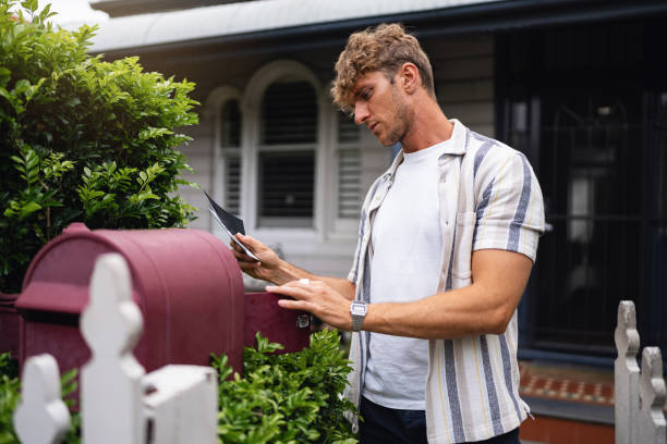 istock Young Man Checking Mail at Red Mailbox in Front of Residential Home 2197781198