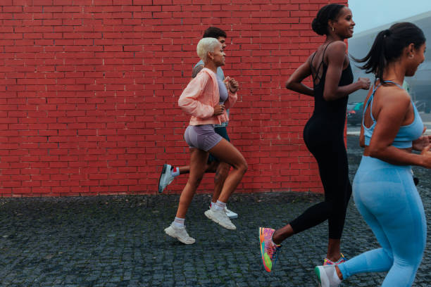 Four athletes are running outdoors, enjoying their workout against a vibrant red brick wall