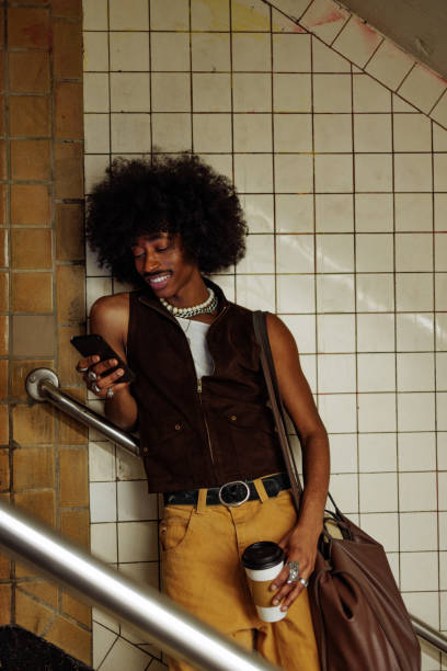 Stylish young man using phone and drinking coffee in subway station