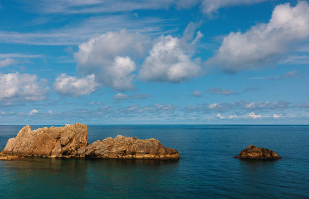 Rocky islands emerging from the calm blue ocean under a sky filled with fluffy white clouds