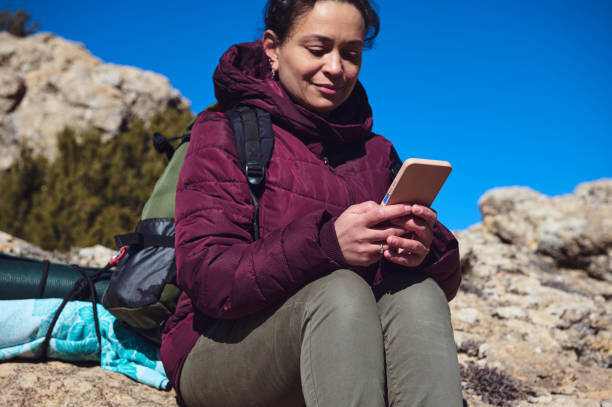 istock Woman sitting outdoors checking phone during hiking trip, enjoying nature 2197802117