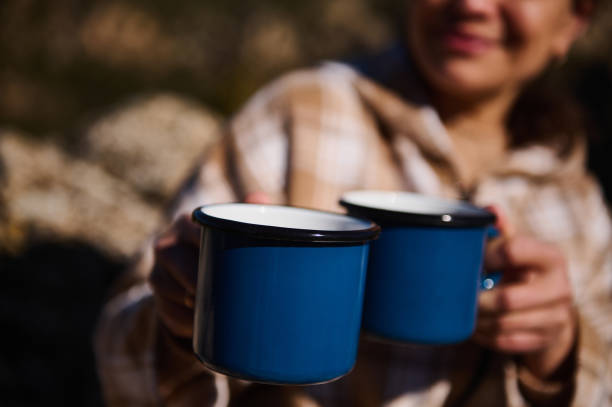 istock Person Holding Two Blue Metal Mugs Outdoors in a Scenic Camping Setting 2197802202
