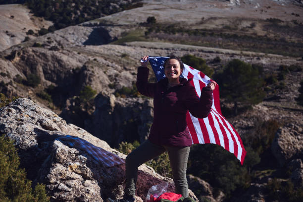 istock Confident woman holding an American flag while standing on a rocky hill under a bright sky 2197802880