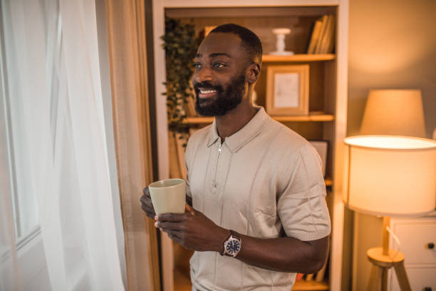 istock A handsome black man looks out the window while drinking his first morning coffee 2197804443