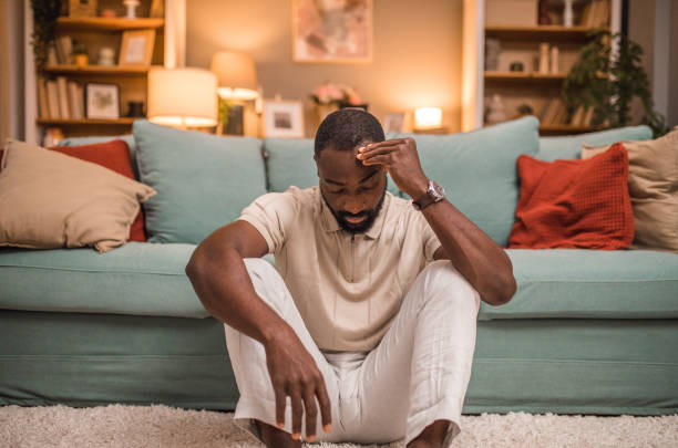 istock Black man sitting on living room floor with severe headache 2197804700