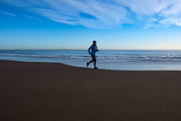 Senior woman running on the beach just north of Aberdeen, Scotland, as dawn breaks. With the tide going out, the sand is free of footprints.