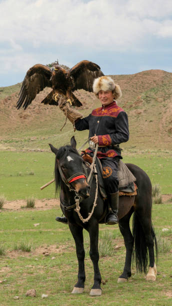 Issyk Kul, Kyrgyzstan - 23 May 2022: Eagle trainer on horseback with his golden eagle, showcasing traditional hunting techniques passed down through generations.