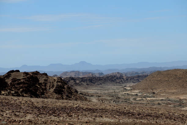 There is a dirt road on the right leading into canyons. In the distance  the millions of years old Doros Crater. T\nThe photo was taken in the Doros !Nawa Conservancy in Damaraland in the Kunene Region of Namibia in February 2024