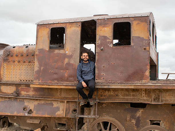 Traveler man posing in an old rusty locomotive in Uyuni's train cemetery Bolivia