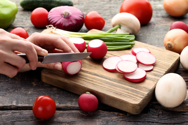 istock Female hand cutting fresh radishes on brown board 2197825803