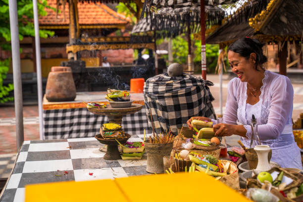 Bali, Indonesia - November 29, 2023: A serene temple scene featuring a woman arranging ceremonial offerings, symbolizing devotion and cultural tradition.