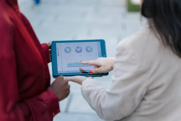 Business colleagues reviewing financial data and charts on a digital tablet, discussing market trends and performance