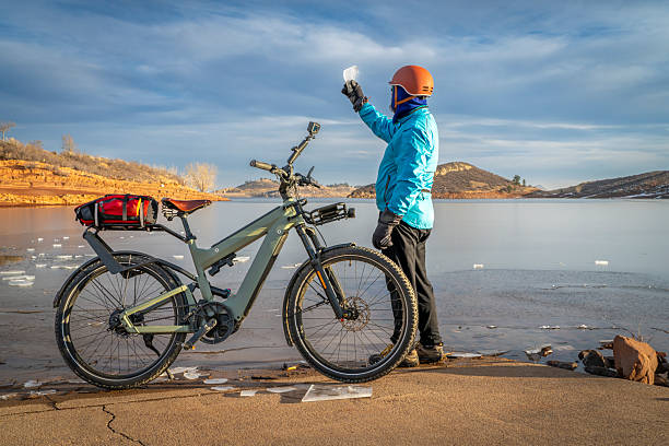 Senior cyclist with a touring e-bike with action camera mounted on handlebar at shore of frozen Horsetooth Reservoir in Colorado foothills.