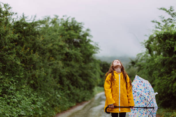 A little girl is playing in the rain, splashing in puddles and holding a toy
