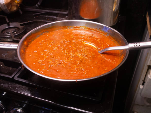 A simmering pot of rich, meaty sauce on a stovetop. The vibrant red color and texture suggest a hearty, flavorful dish.