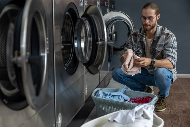 istock Man in laundromat holding washed clothes after using coin-operated appliance 2197861309