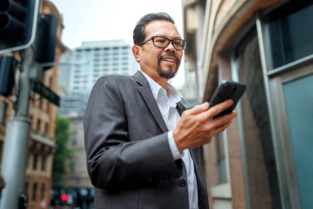 istock Smiling mature businessman texting on smart phone while enjoying day outdoors in Sydney 2197869031