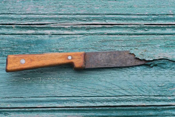 one old knife with a black blade and a brown handle sticks out of a green wooden wall on a summer street