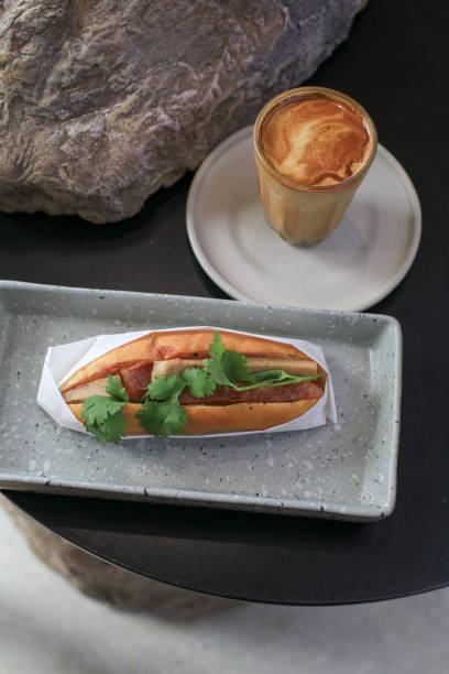 Banh Mi Vietnamese Sandwich, grilled pork and fresh vegetable eating with coffee on black rock in coffee shop.