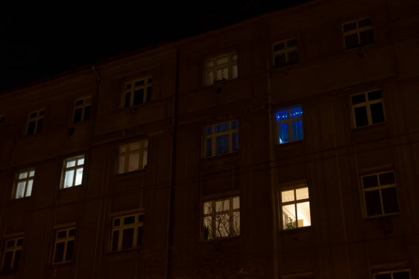 A tall and modern building filled with numerous windows is brightly illuminated during the night, casting a warm glow amid the darkness