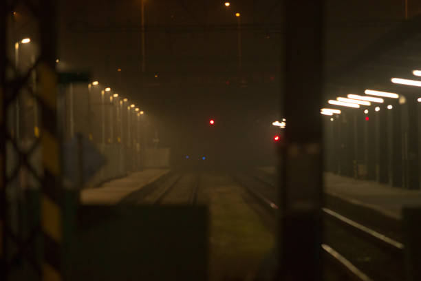 A foggy train station platform displays a scene of tranquil tracks, dim lights, and shadowy surroundings, evoking a quiet commute atmosphere