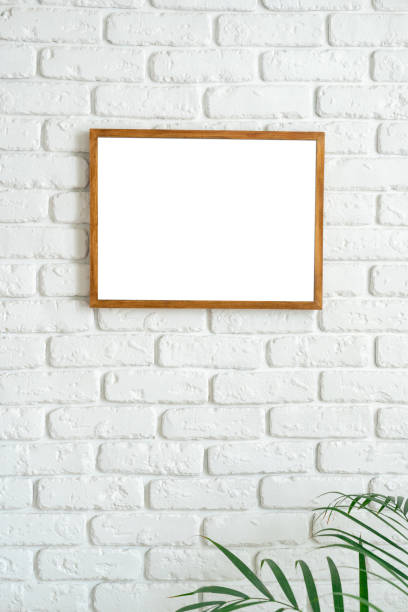 istock Blank wooden frame on white brick wall with plant in the lower corner capturing minimalism in interior design 2197916438