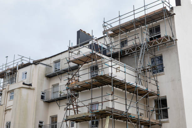 Scaffolding is set up against a building facade currently under renovation, revealing unfinished plaster and windows