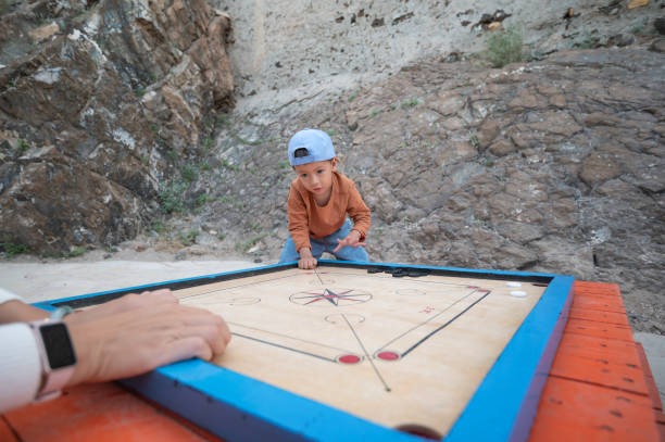 A child plays a Carrom tabletop game with deep concentration against a rugged background, showcasing youthful determination and the joy of play in natural settings.
