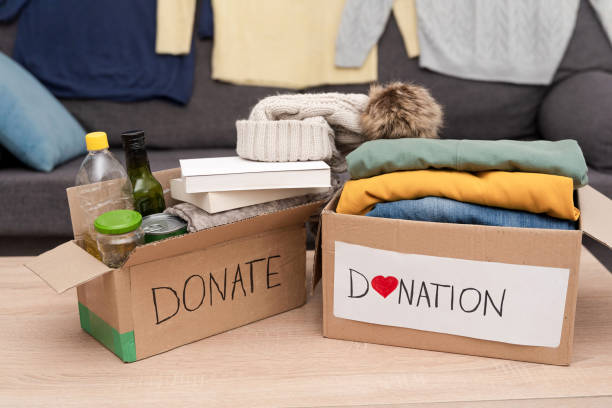 istock Two Donation boxes with food, clothes and other necessities on table for charity and some clothes on sofa 2197922005