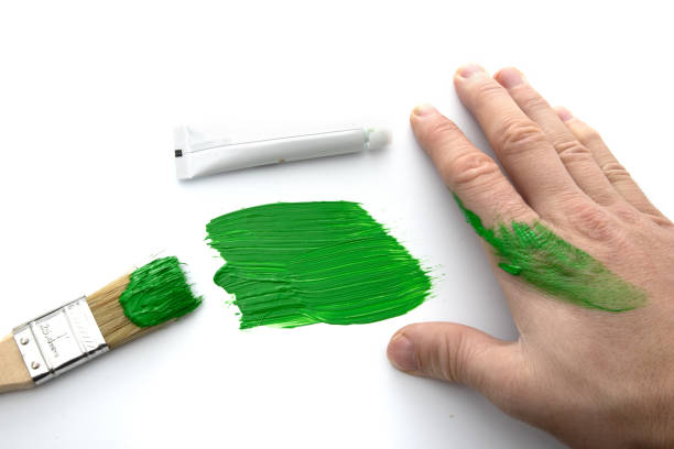 Hand smearing green paint with brush and tube nearby