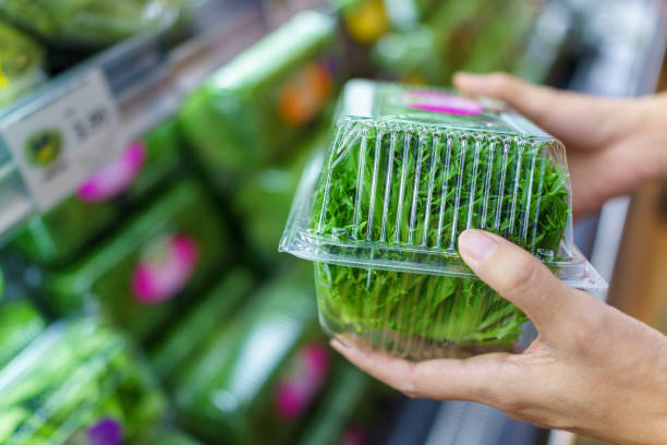 Shopper examining a plastic container of fresh leafy greens in the supermarket vegetable aisle.