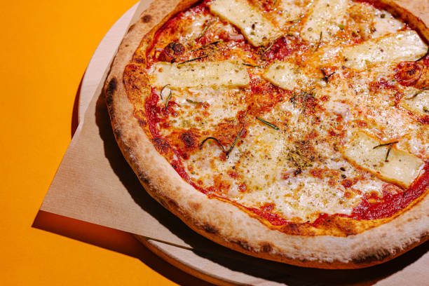 istock Freshly baked cheese pizza with herbs on a bright orange table ready to be enjoyed 2197928122