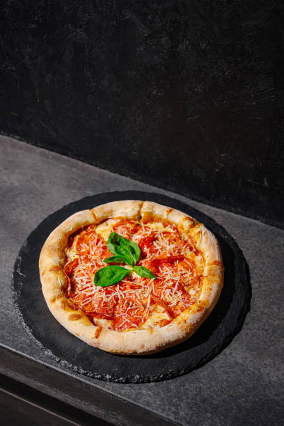 Classic margherita pizza with fresh basil on a dark stone surface in a warm kitchen setting topped with grated cheese