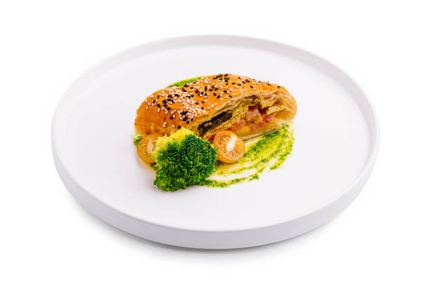 A gourmet pastry filled with vegetables is elegantly arranged on a minimalist white plate, accompanied by fresh broccoli and a vibrant green sauce, showcasing fine dining creativity.