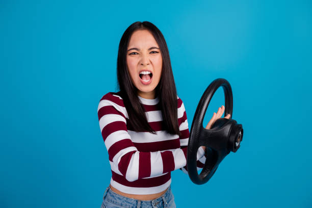 istock Energetic young woman expressing frustration while holding a steering wheel against a vibrant blue background 2197933581