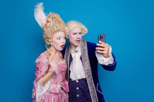 istock A historical couple dressed in elegant vintage attire looks surprised while taking a selfie against a vibrant blue background 2197934661