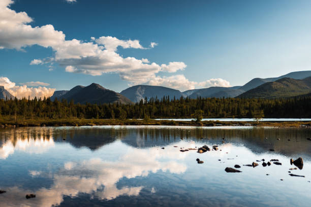 Scenic landscape of a calm lake reflecting mountains and lush forests under a clear sky
