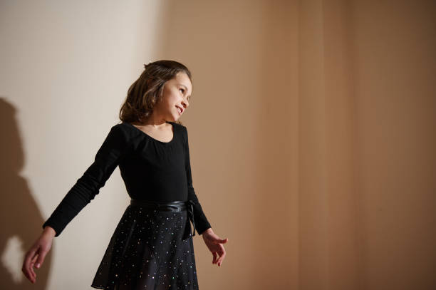 Portrait of a girl dressed in a fitted black top and shimmering skirt, standing indoors. The soft lighting creates a peaceful ambiance, enhancing her poised expression and stylish outfit.