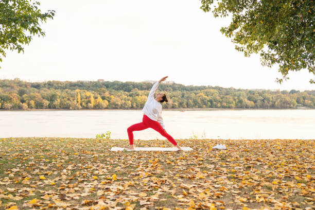 woman practicing yoga outdoors in nature next to river in autumn