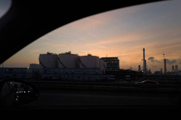 Industrial complex silhouetted against a colorful sunset, seen through a car window on a highway