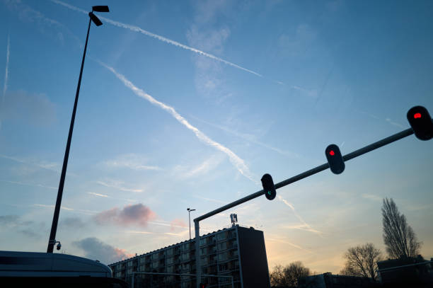 Traffic lights glow red as contrails streak across a serene evening sky above a cityscape