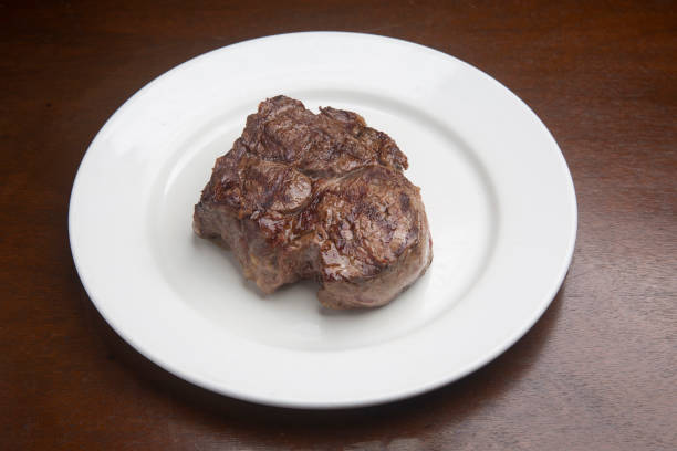 Juicy grilled beef steak resting on white ceramic plate over rustic wood surface