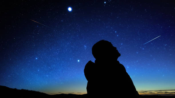 istock Silhouette of a man observing Milky Way stars, planets and other celestial objects from a dark countryside location. 2197942079