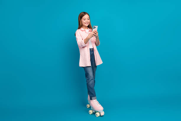 istock Trendy girl using a smartphone while standing in pink roller skates against a blue background 2197942527