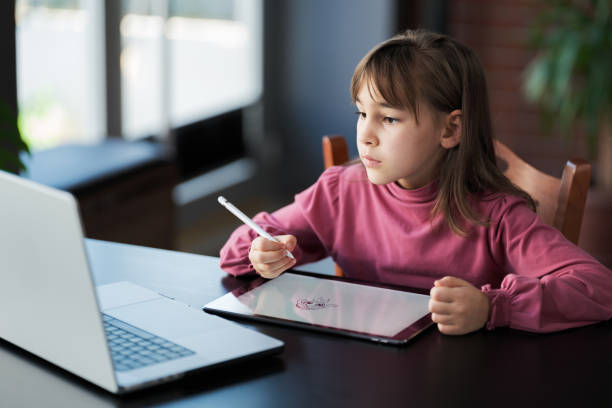 istock Child girl watching online tutorial on laptop computer and drawing digital pictures using digitized pen and digital tablet 2197943344