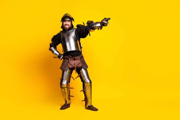 A joyful young man dressed as a medieval knight with full armor, playfully pointing against a yellow backdrop, combining history and fun in a vibrant scene.