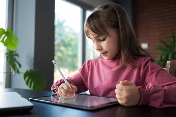 Child girl watching online tutorial on laptop computer and drawing digital pictures using digitized pen and digital tablet