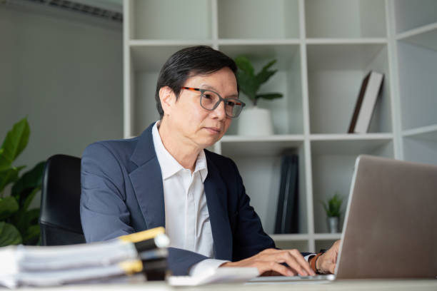 Elderly businessman working in modern office engaged in digital tasks professional environment focused viewpoint An elderly businessman focuses intently on digital tasks in a modern office setting showcasing dedication to his work. legacy concept stock pictures, royalty-free photos & images