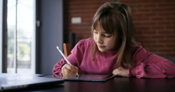 istock Child girl watching online tutorial on laptop computer and drawing digital pictures using digitized pen and digital tablet 2197944164