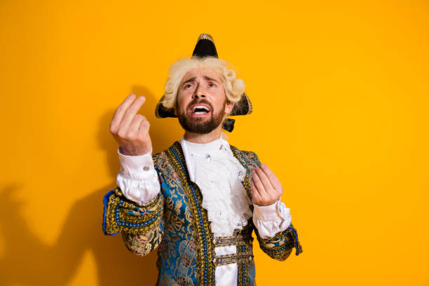 Retro baroque man with white wig holding a walking stick sitting on antique couch. Studio shot against blue.